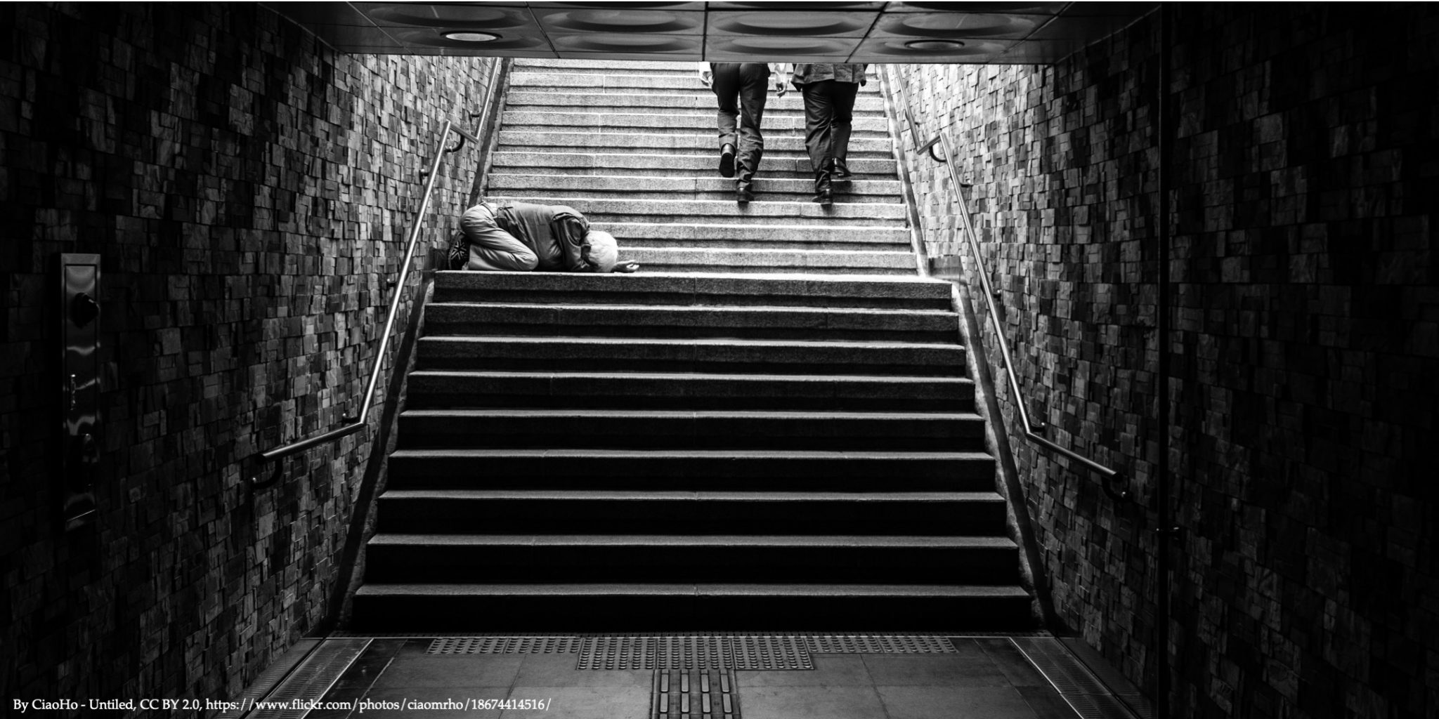 A black and white image of man begging for help in a dark tunnel representing global inequality