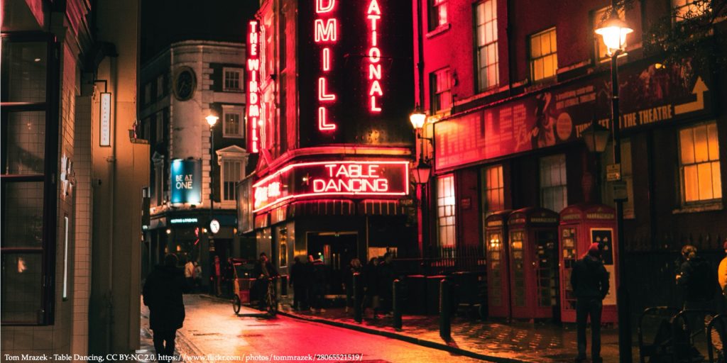 An image of red light street with signs of striptease club representing human trafficking and prostitution legislation