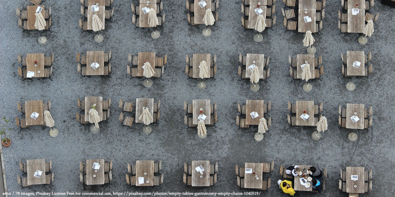 Areal image of empty restaurant tables with only one table occupied by two people representing governance and Covid-19