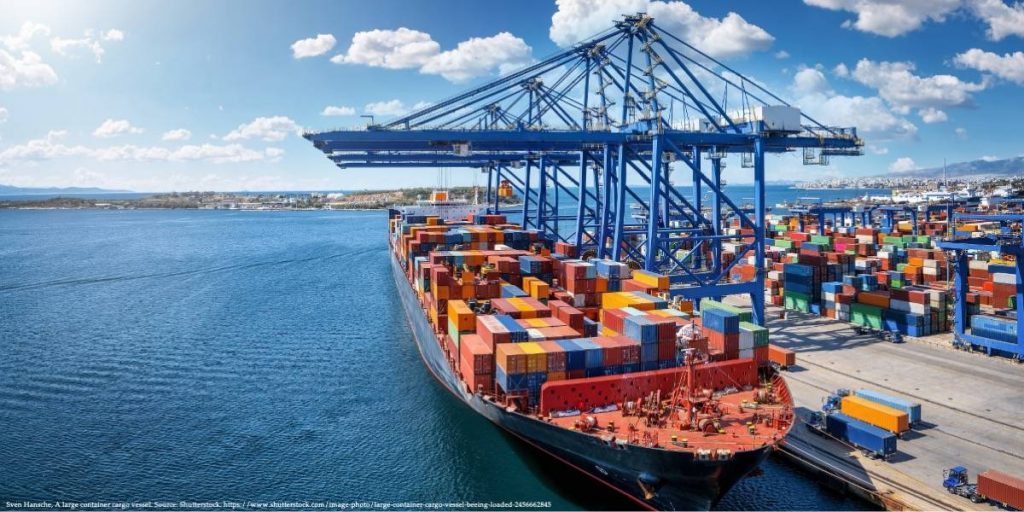 Large container cargo vessel being loaded at a deep sea port with cranes, colorful shipping containers, and a clear blue sky