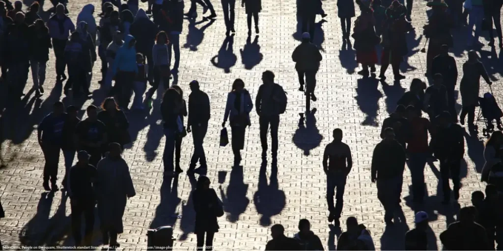 Silhouetted crowd of people walking in a public square, symbolizing societal impacts of the gender gap in life expectancy.