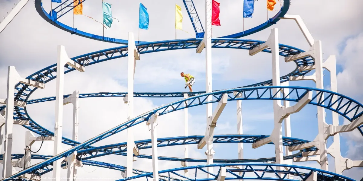 A person performing high-altitude cleaning on a roller coaster structure, symbolizing bravery and entrepreneurship spirit in Belarus, with future generations and children in mind.